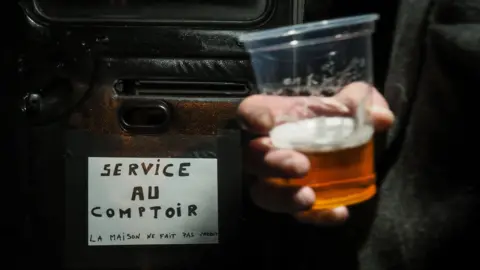 A man holds a glass at a bar truck in the village of Villequiers, central France. Photo: March 2019