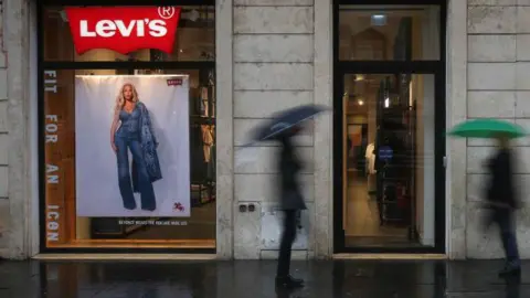 Two men with umbrellas, blurred in the photo, walk past a shop selling Levi's jeans