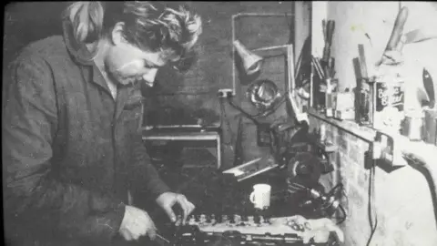 Ros Wollen A female mechanic pores over a workbench in a monochrome picture.