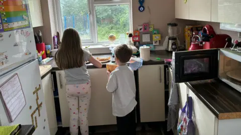 Kirstie Two children facing away from the camera making breakfast in a kitchen