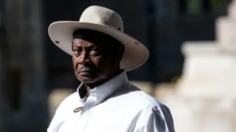 Getty Images Uganda's President Yoweri Museveni wears a white shirt and a matching wide-brimmed hat. 