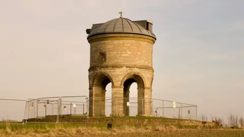 Chesterton windmill without it sails and surrounded by security fencing.