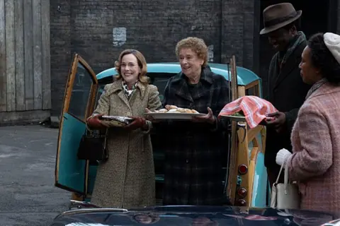 BBC/Neal Street Productions Nurse Shelagh Turner (Laura Main), Nurse Phyllis Crane (Linda Bassett) and Cyril Robinson (Zephryn Taitte) dishing out food from the back of a car in the East End