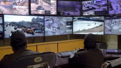 Two people sit in a CCTV control room