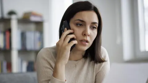 Woman holds smartphone to ear and looks concerned