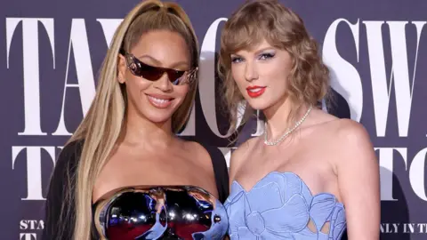 Getty Images Beyoncé and Taylor Swift pose at the US premiere of Swift's concert movie in 2023; both are in strapless gowns and are smiling