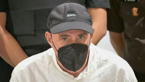 A man wearing a white shirt, a black cap and a black face mask