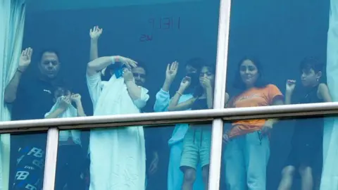 Getty Images Young and old migrants in the Decápolis hotel stand at a window and try to catch the attention of those outside