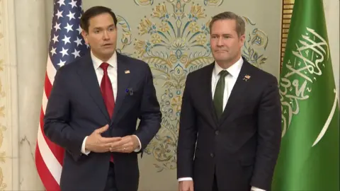 US Secretary of State Marco Rubio speaking wearing a blue suit and red tie and National Security Adviser Mike Walt