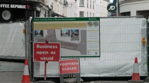 BBC Metal gate with signs and a large banner on a white sheet covering the gate.