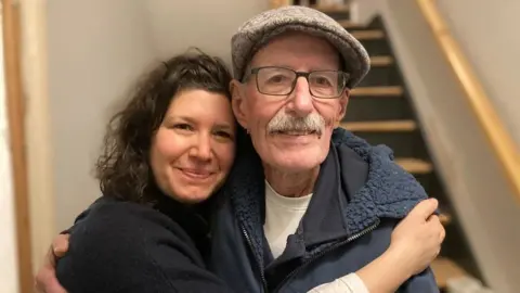 LIFSCHITZ FAMILY Sharone and Oded hugging each other and smiling. Photo taken in a house. 