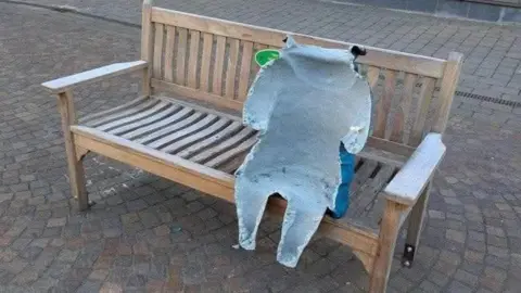 The defaced statue of Paddington on its bench. Only part of it is left, with the front completely torn off. 