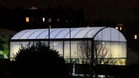 Max Mitchell I very brightly lit indoor tennis court building glowing in the dark.