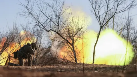 A Ukrainian soldier covers his ears as a howitzer fires in the Zaporizhzhia region of Ukraine