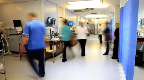 A slightly blurred image of a hospital corridor with staff in uniform walking past in different directions. 