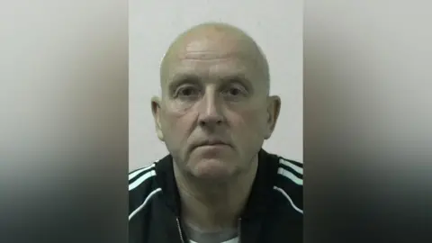 Northumbria Police Mugshot of Michael Stewart. He is bald and clean shaven and is wearing a black jacket with white stripes running down the arms