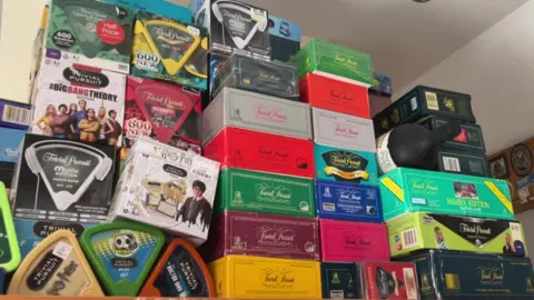 BBC/Nathan Turvey Several boxes of the Trivial Pursuit board game stacked on top of each other.