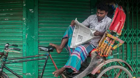 A rickshaw driver reading a newspaper