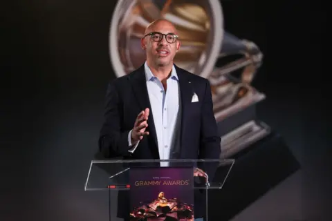 Getty Images Harvey Mason, Jr standing at a podium in a jacket and shirt 