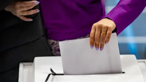 A woman in a purple top casts her ballot for parliamentary elections at the polling station in Nuuk, Greenland