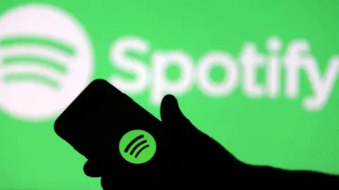 A smartphone is seen in front of a screen projection of Spotify logo