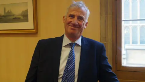 Lord Storey Lord Storey, who has grey hair and wears a blue suit over a white shirt, smiles at the camera 