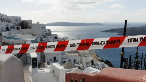 An image of Santorini's white picturesque buildings with red tape. 