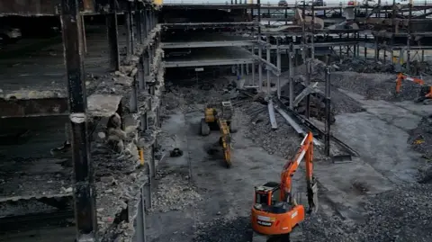 A digger stands in the charred wreckage of a multi-storey car park at Luton Airport.