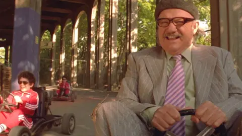 Gene Hackman in character in the Royal Tenenbaums smiling while driving a Go Kart