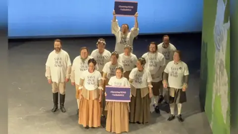 Cast display tee-shirts saying Save Our WNO and wave placards