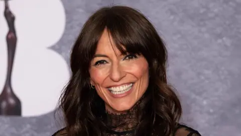 Davina McCall is smiling while posing on a red carpet.