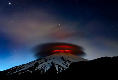 Francisco Negroni / Wildlife Photographer of the Year A fiery red glow from Chile’s Villarrica volcano illuminates the night sky. Above it, a lenticular cloud takes on an eerie, swirling shape, glowing in the reflected light.