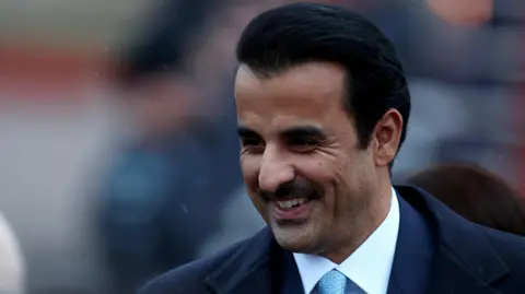 Reuters Emir of Qatar smiling while wearing a suit with a light blue tie in the rain. He has short black hair and a black moustache.