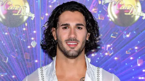 PA Media Graziano Di Prima standing in front of a backdrop showing Strictly logos and glitterballs