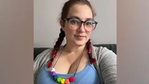 Kirstie Kirstie looking at the camera, with two plaits, wearing a colourful necklace