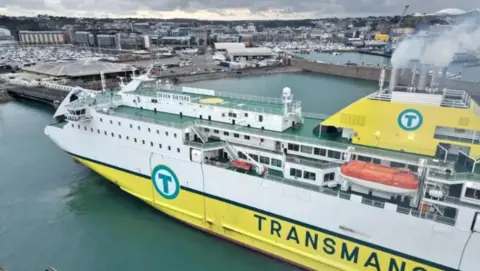 A yellow and white ship with green decks and smoking funnels in a harbour.