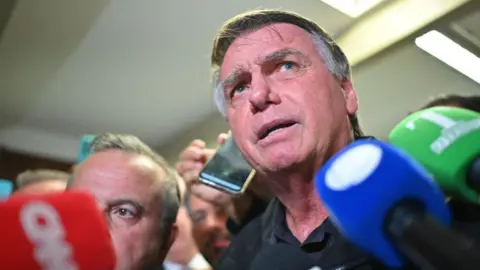 Getty Images Jair Bolsonaro speaks to journalists on Tuesday, surrounded by red, blue and green microphones.