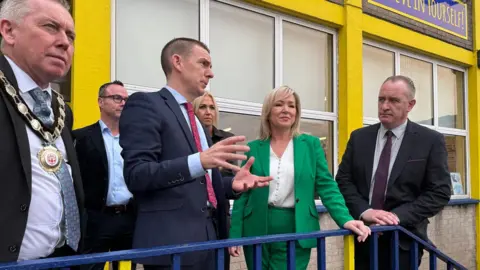 Michelle ONeill attends an event at a school in Magherafelt. She stands outside the school with the principal and mayor discussing the school. 