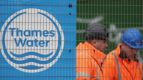 EPA Thames Water workers wearing hard hats behind heras fencing