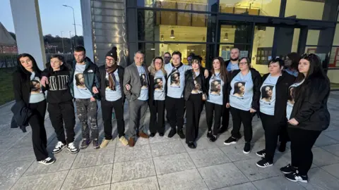 George King/BBC About 14 members of Courtney Mitchell's family standing outside Ipswich Crown Court. They are all wearing blue t-shirts with Ms Mitchell's face printed on them.