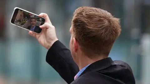 PA Media Alex Belfield taking a picture of himself outside Nottingham Crown Court during his trial in July 2022.