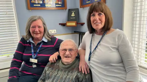 Phil Harrison/BBC Retired Group Captain Keith Reyner and volunteers Marion Cruse and Kim Buttenshaw sit in lounge at the Royal Navy Benevolent Trust's Pembroke House care home in Gillingham