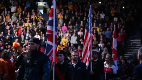 PA The three flags of the UK, USA and Canada paraded at the closing ceremony with a large crowd in the background