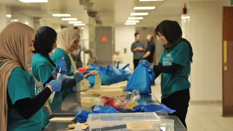 Kashif Darr Charity volunteers wearing blue t-shirts and headscarves preparing food bags 