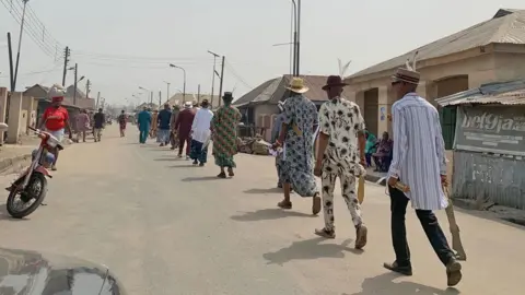 Adaobi Tricia Nwaubani Members of the Igbuu Society seen walking down a street in Oguta in single file each holding a gold sword