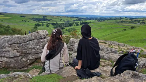 Bradford 2025 Two young women sat down facing a green field 