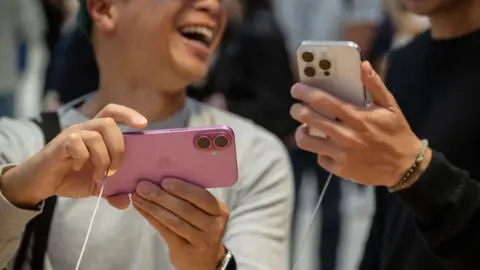 Customers hold Apple iPhone 16 and 16 Pro in a shop