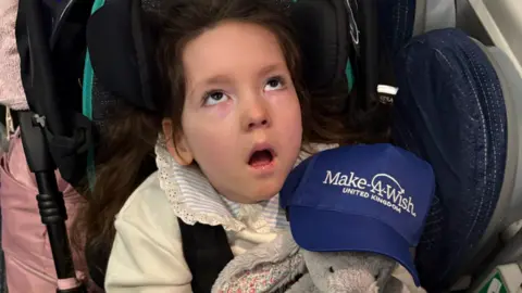 Toni Mannion An image of a young girl looking upwards with a cuddly toy on her lap. A hat wiith the words 'Make-A-Wish' United Kingdom'  is also seen in the photograph 