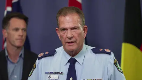 David Hudson, a man in light blue police uniform with short blonde hair, addresses a news conference.