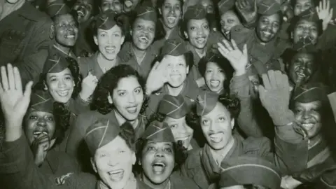 US Army Members of the 6888th Central Postal Directory Battalion look towards the camera and smile and wave